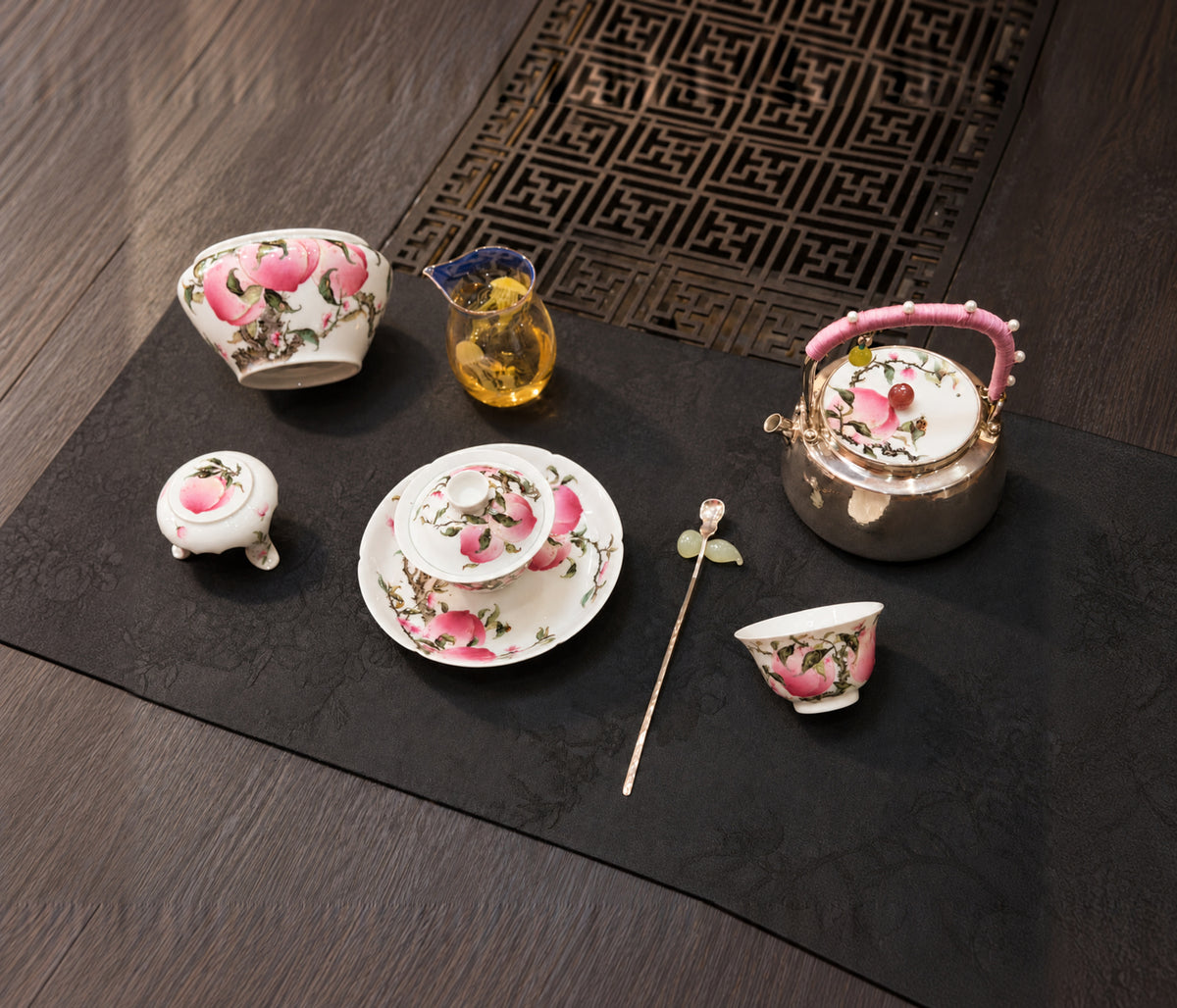 Peach-decorated teapot, bowls and cups arranged on a dark table