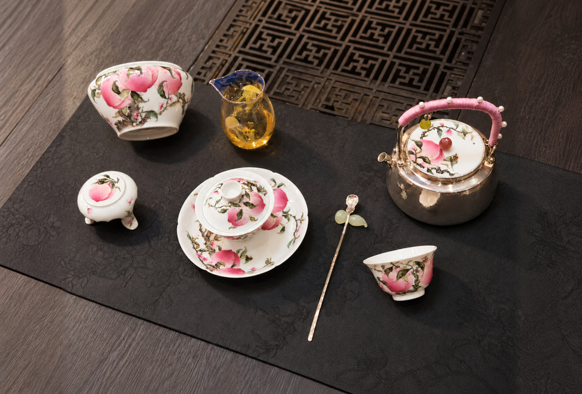Peach-decorated teapot, bowls and cups arranged on a dark table