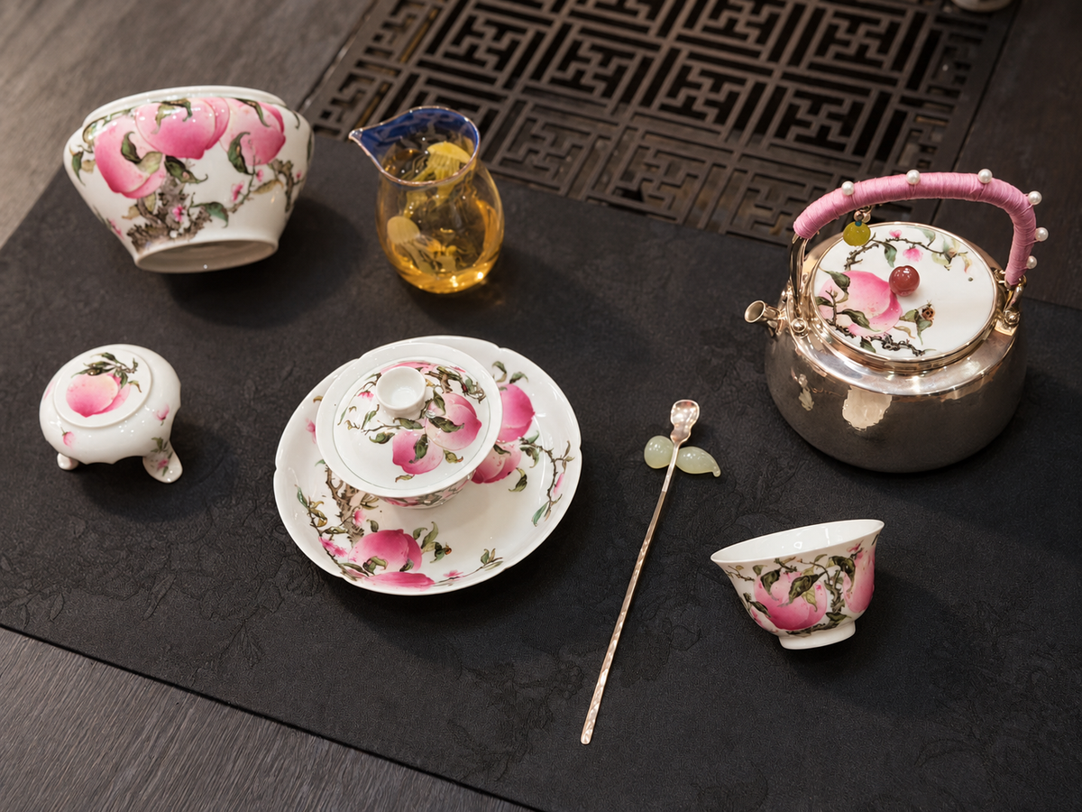 Peach-decorated teapot, bowls and cups arranged on a dark table