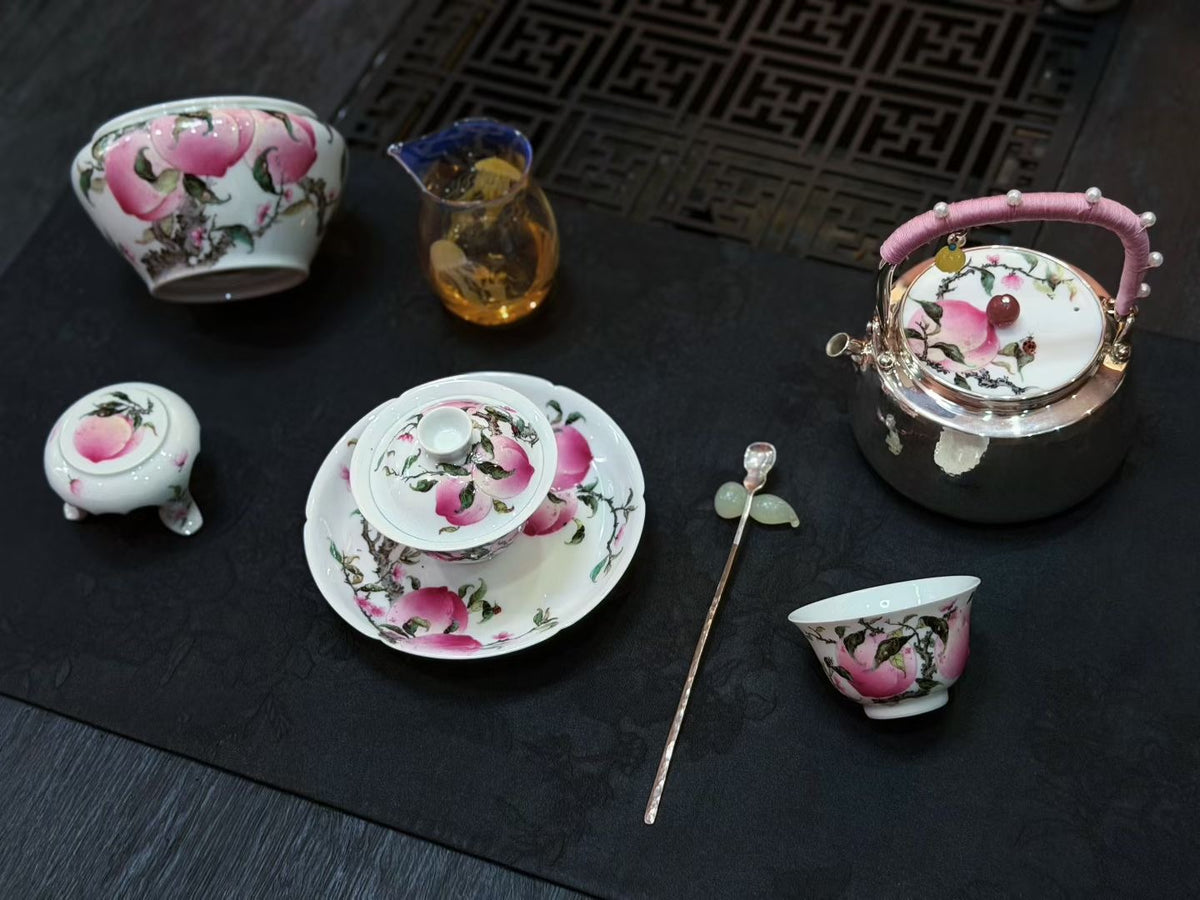Peach-decorated teapot, bowls and cups arranged on a dark table